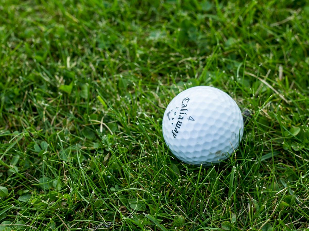 A white golf ball is resting on green grass, with "Callaway" written on it.