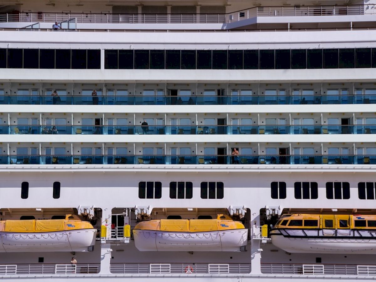 The image shows the side of a cruise ship with lifeboats attached and balconies above.