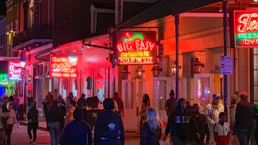 A busy street at night with people walking by brightly lit neon signs for restaurants and bars, creating a lively atmosphere.