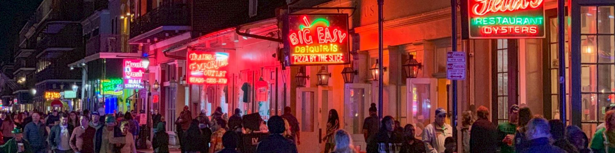 A busy street at night with people walking by brightly lit neon signs for restaurants and bars, creating a lively atmosphere.