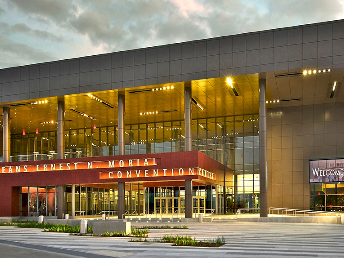 This image shows the exterior of the New Orleans Ernest N. Morial Convention Center, featuring modern architecture under a cloudy sky.