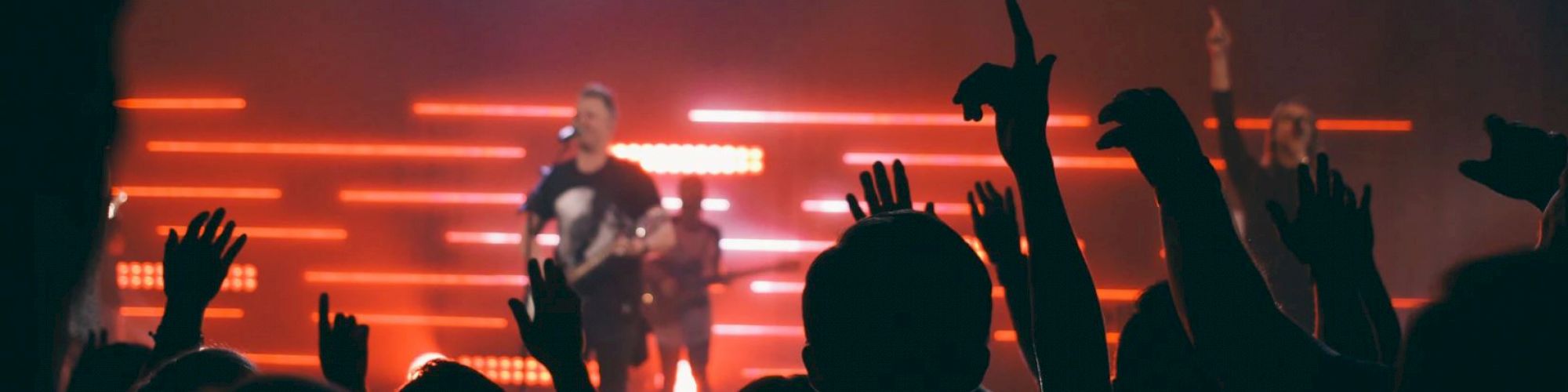 A concert scene with a band performing on stage, vibrant lighting, and a crowd of people raising their hands, creating an energetic atmosphere.