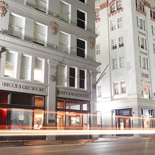 A city street at night showing a long-exposure photo of two buildings with one labeled "Queen & Crescent."