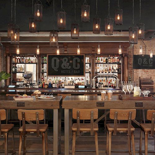 This image shows a bar interior with wooden stools, hanging lights, and shelves stocked with various bottles. The bar's sign reads "O&C Hotel & Bar."