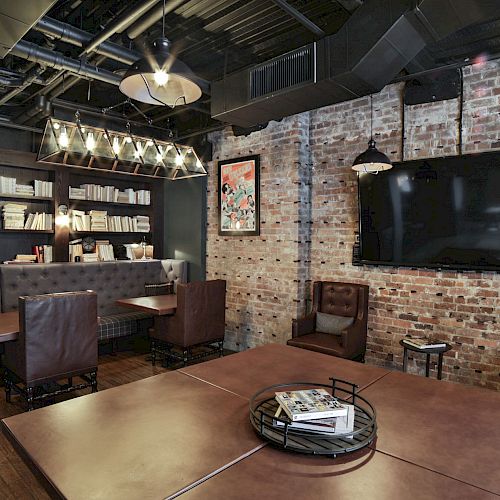 A cozy, modern lounge with leather seating, bookshelves, a large TV on a brick wall, and ambient lighting, creating a warm and stylish atmosphere.