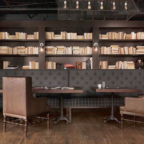 The image shows a cozy seating area in a cafe or library with bookshelves, leather chairs, and wooden tables over a dark, stylish decor.