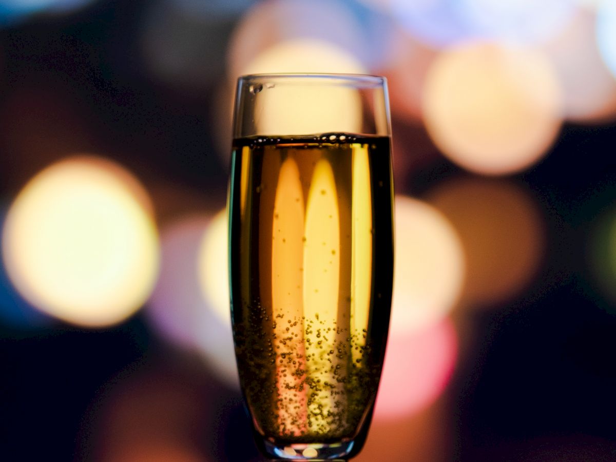 A champagne flute filled with sparkling wine is in the foreground with colorful bokeh lights in the background.