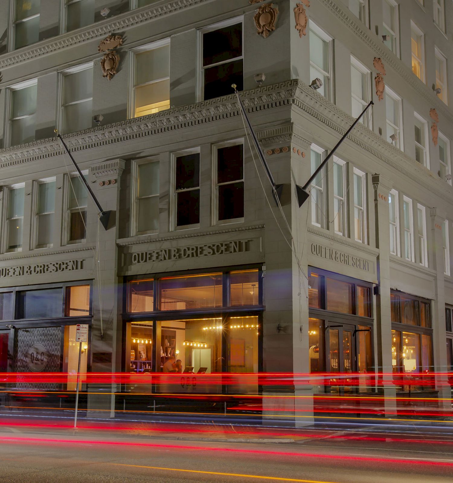 This image shows a corner building illuminated at night, with light trails from passing vehicles. The bottom floor appears to be a commercial space.