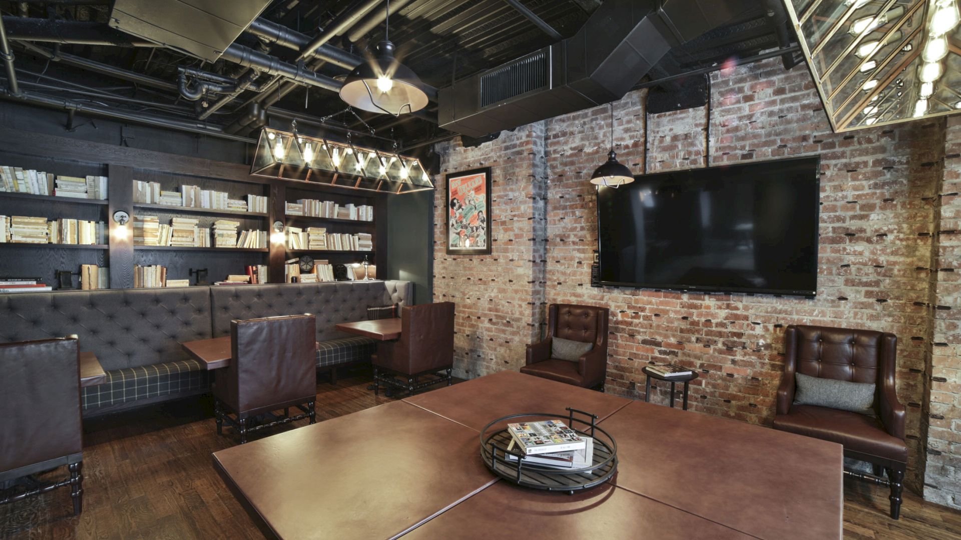 A modern lounge with leather chairs, bookshelves, a large TV, exposed brick walls, and industrial lighting, creating a cozy, contemporary ambiance.
