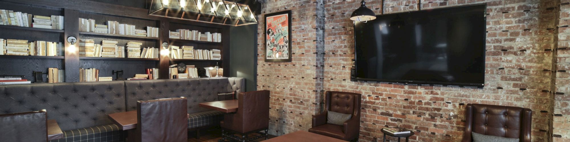 A modern lounge with leather chairs, bookshelves, a large TV, exposed brick walls, and industrial lighting, creating a cozy, contemporary ambiance.