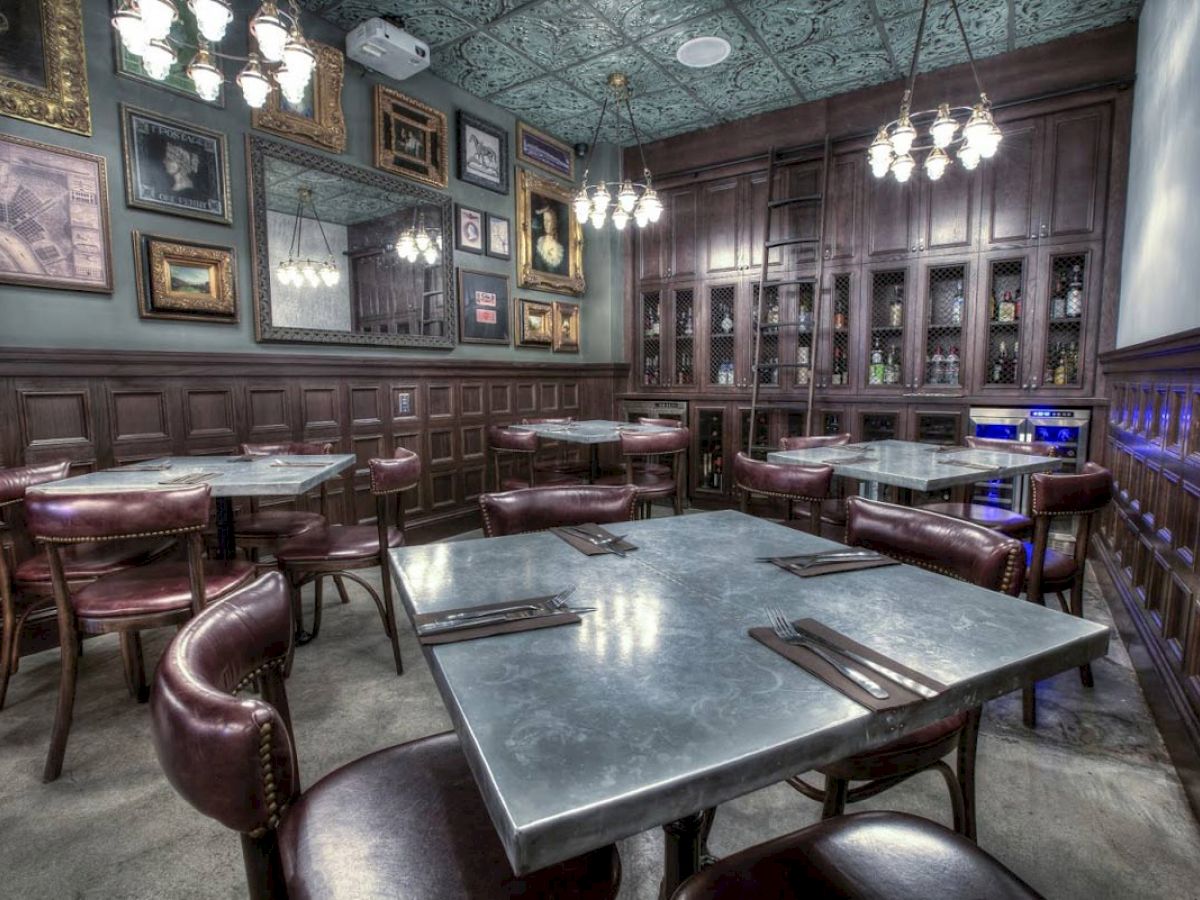 This image shows a stylish, empty restaurant with modern decor, framed art on the walls, metal tables, and brown leather chairs with dim lighting, ending the sentence.