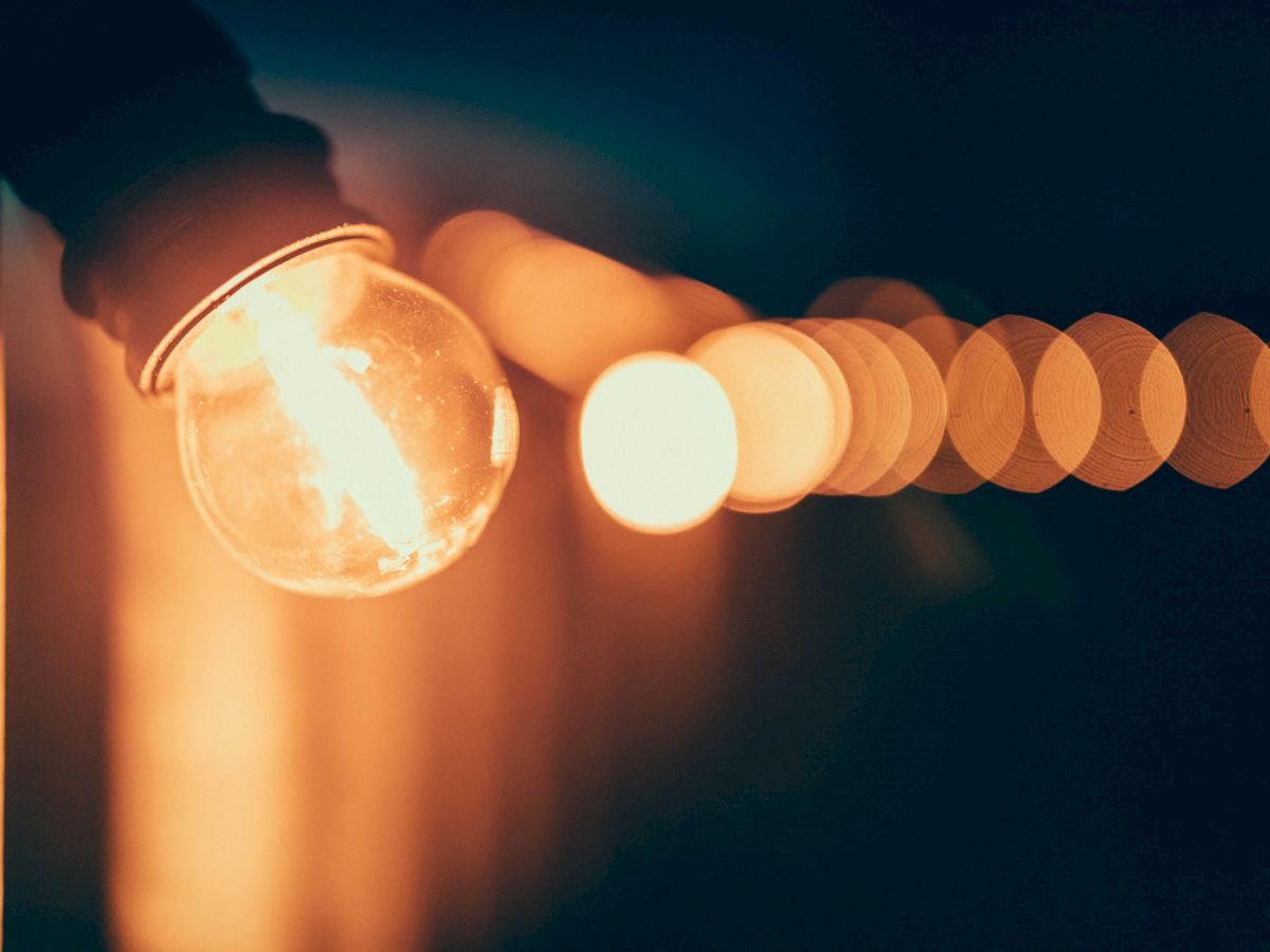 A string of glowing light bulbs, with one bulb in focus in the foreground and the rest blurred in the background, creating a warm ambiance.