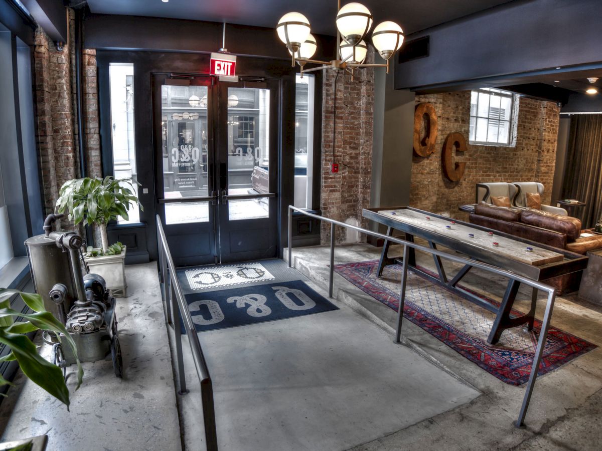 The image shows a stylish indoor space with double glass doors, a rug with "OBC" text, ceiling lights, plants, and a mix of brick and modern decor.