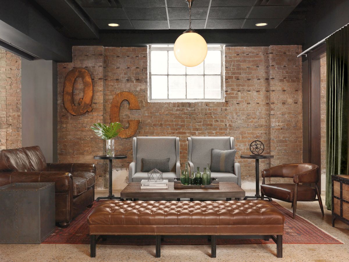 A stylish living room with brown leather and gray seating, exposed brick walls, a window, and modern decor including a large "QC" wall art piece.