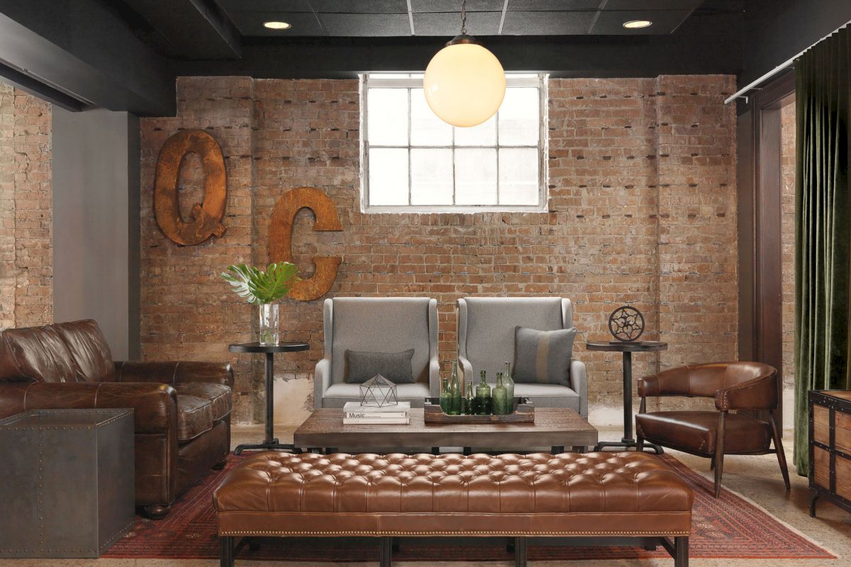 A cozy living room with leather seating, brick walls, decorative metal letters, a central coffee table, plants, and a hanging light fixture.