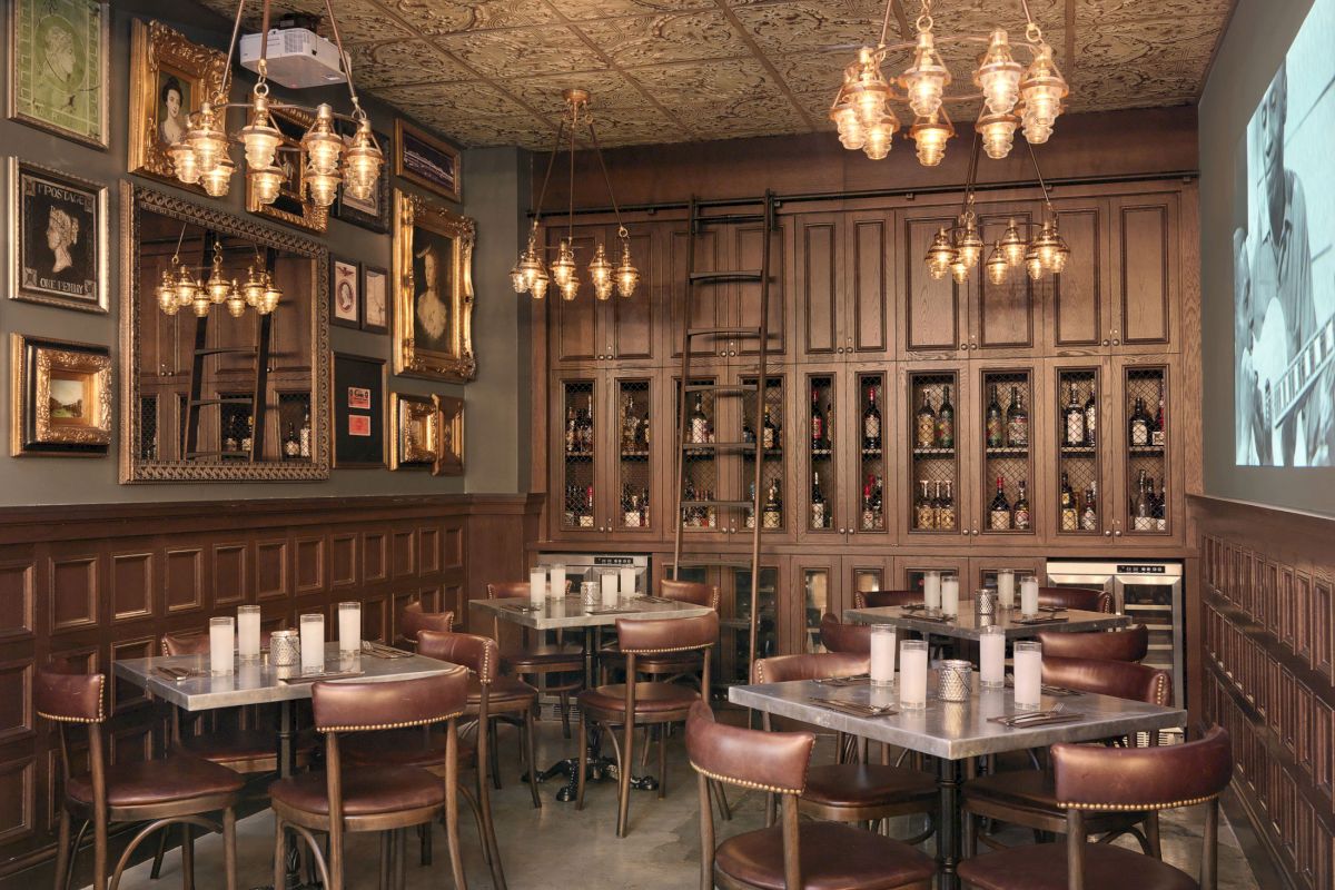 The image shows a rustic-style restaurant interior with wooden paneling, vintage lighting, framed pictures, and neatly arranged tables and chairs.