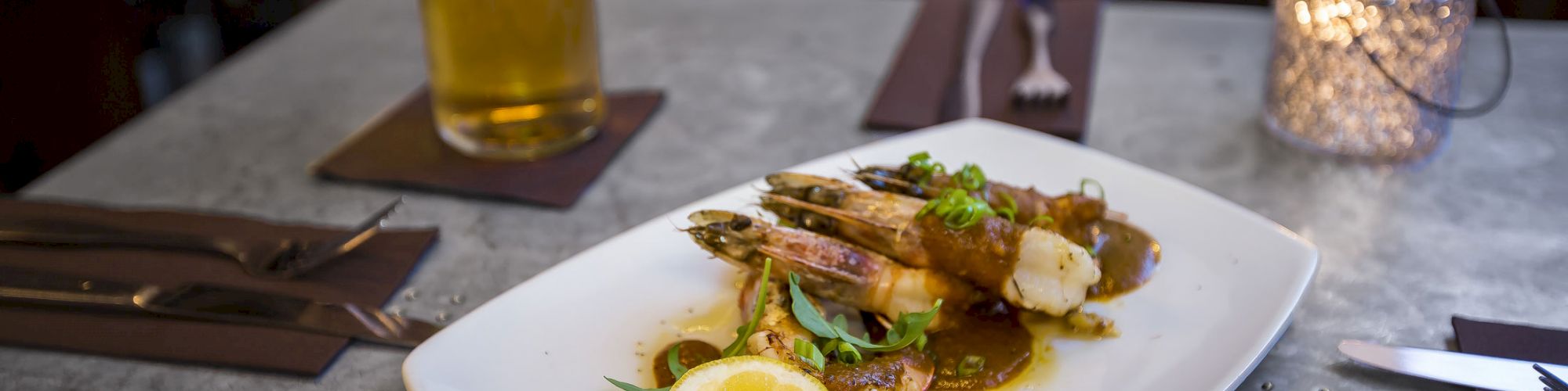 A plate of seafood garnished with a lemon slice, accompanied by a glass of beer, on a table set with utensils and a candle.