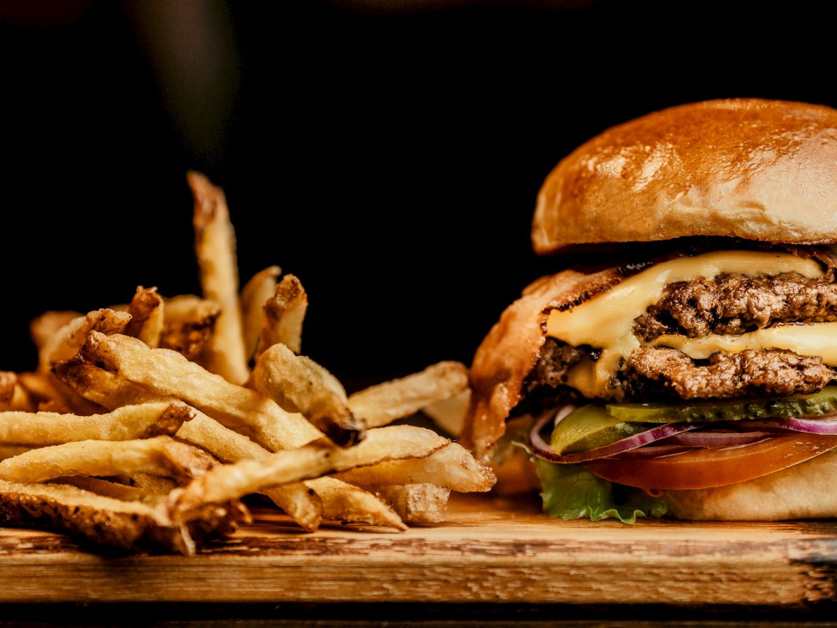 The image shows a cheeseburger with multiple beef patties, melted cheese, and fresh toppings, served alongside a pile of crispy French fries.