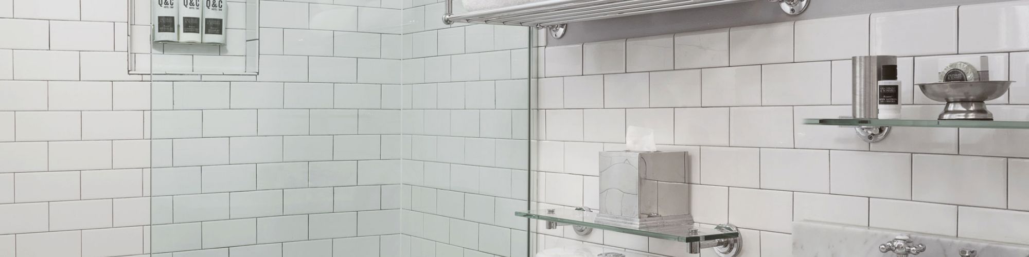 A modern bathroom with a glass shower, white tiles, a toilet, a sink with a mirror, and shelves with neatly stacked towels.