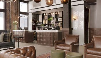 A cozy, modern lounge area with leather sofas and armchairs, a check-in counter, overhead spherical lights, and wooden-paneled decor finishing the sentence.