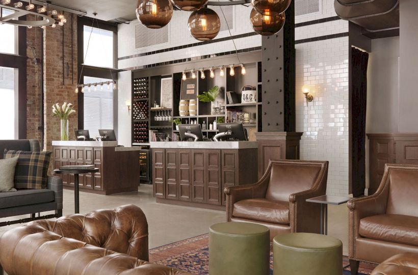 A cozy, modern lounge area with leather sofas and armchairs, a check-in counter, overhead spherical lights, and wooden-paneled decor finishing the sentence.