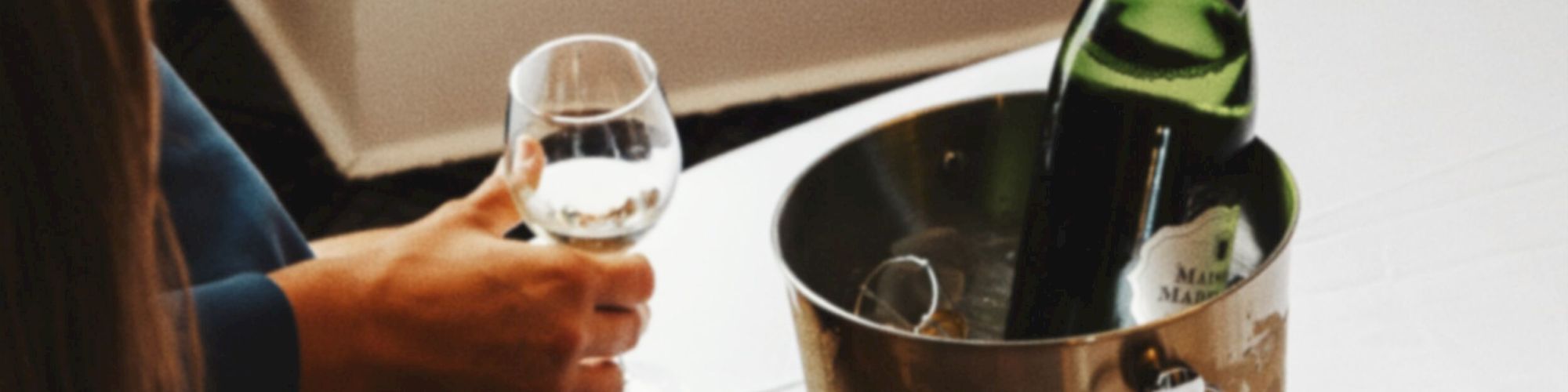 A couple cheers with white wine in a restaurant booth, with a green bottle in an ice bucket on the table.