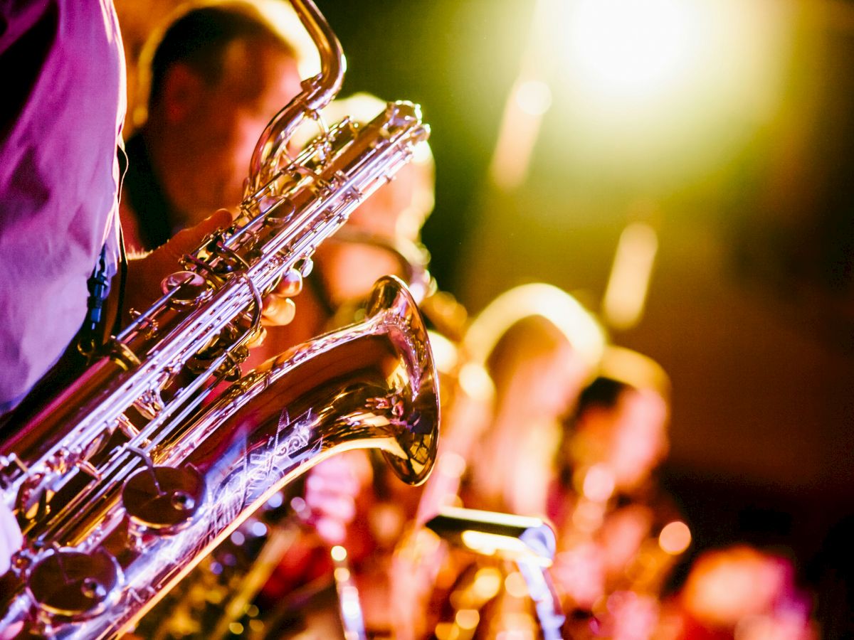 The image shows a group of musicians playing saxophones with bright stage lighting in the background, creating a lively and vibrant atmosphere.