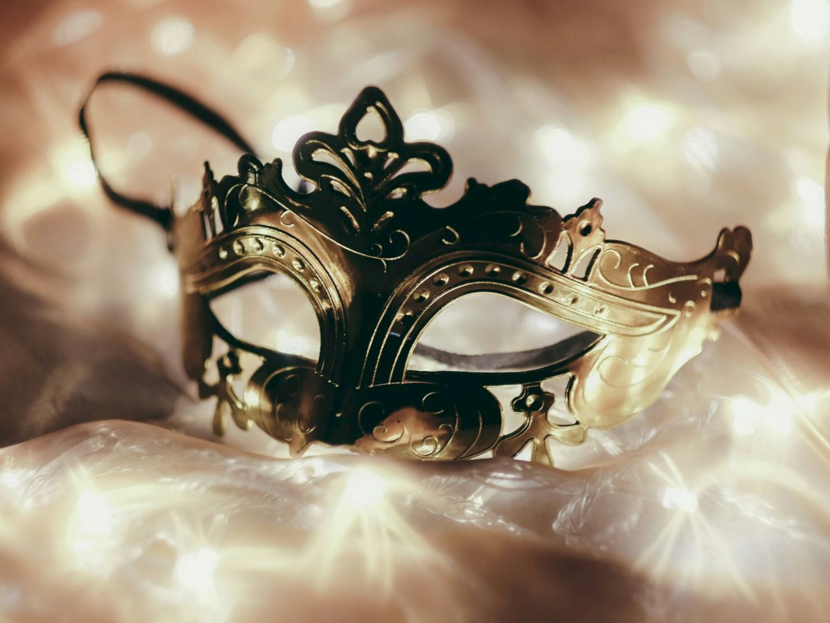 A decorative masquerade mask with intricate designs sits among softly glowing lights, creating a romantic and mysterious atmosphere.
