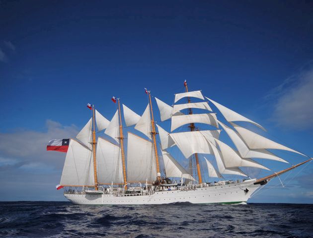 A large white sailing ship with multiple masts and sails cruising on calm blue ocean under a clear sky.