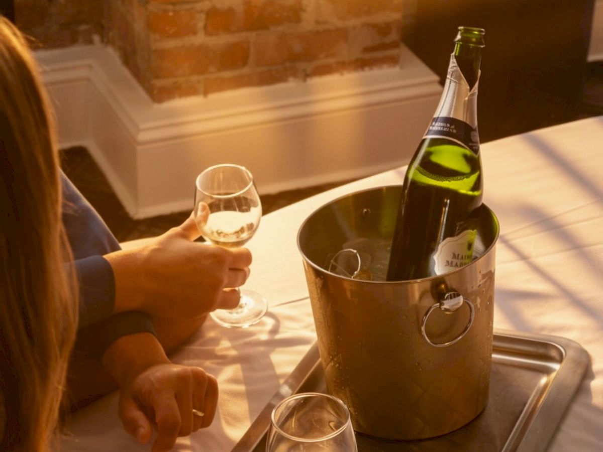 Two people toast with wine glasses on a tray, with a bottle in an ice bucket against a brick wall.
