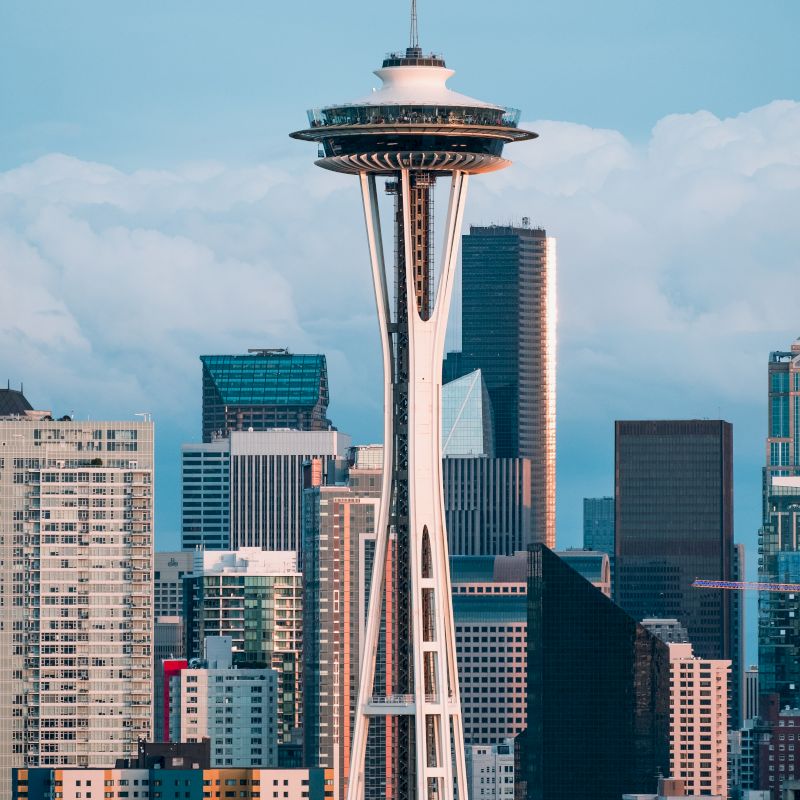 The image shows the Space Needle in Seattle, surrounded by other buildings against a backdrop of a cloudy sky, highlighting an iconic cityscape.