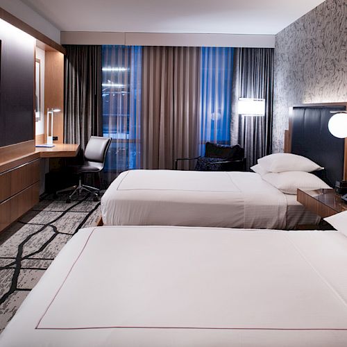 This image shows a modern hotel room with two neatly made beds, a TV on the wall, a work desk with a chair, and stylish decor.